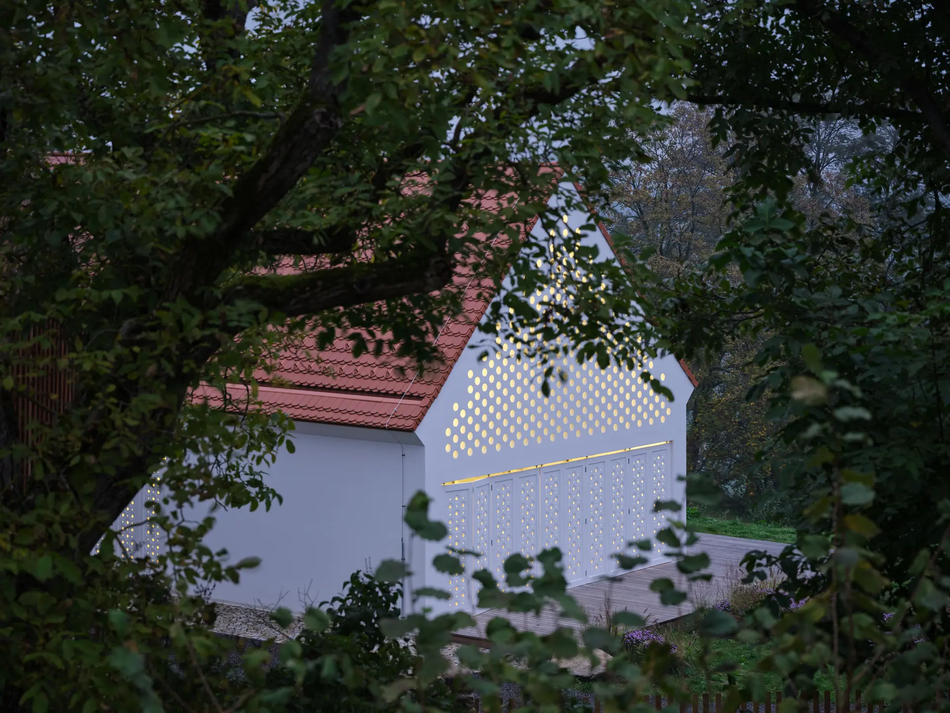 pohled na House Oskar mezi stromy, večerní světlo prosvítá perforovanou fasádou